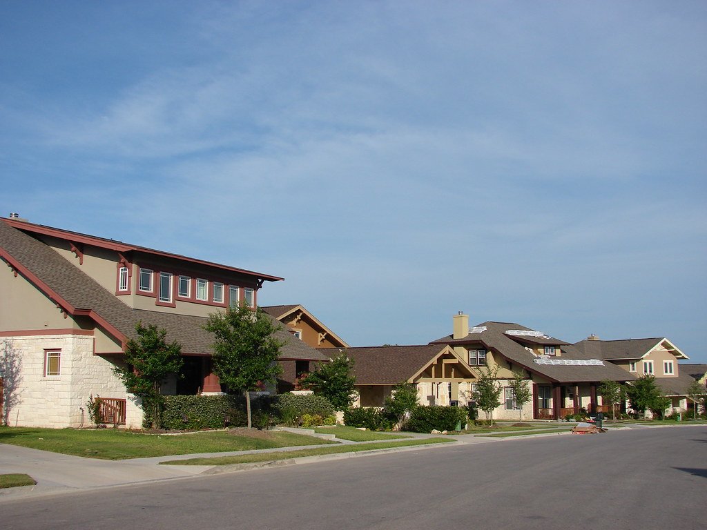 Brick and stone single-family homes with green lawns on a suburban street in Texas, typical of Rosenberg neighborhoods served for pest control