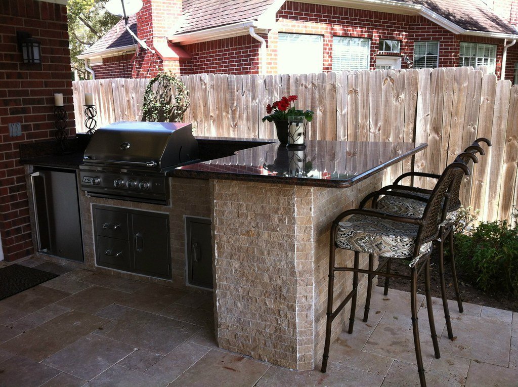 Backyard patio and outdoor kitchen beside a red brick home with a wood privacy fence in Fort Bend County, Texas